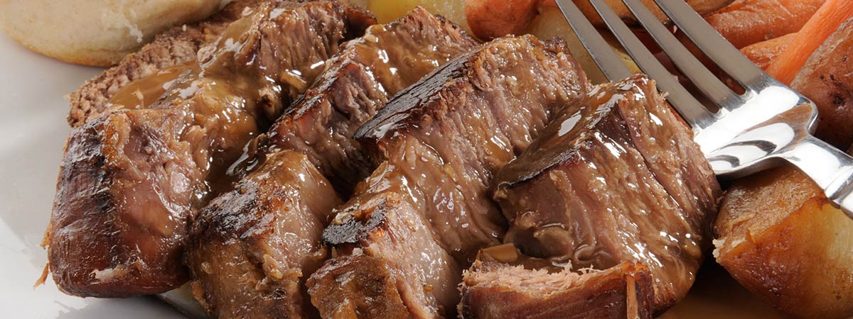 Sliced pot roast with carrots, potatoes, and gravy on a white platter